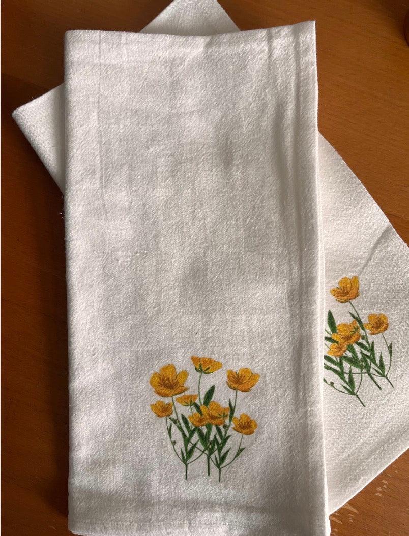 White cotton napkins with yellow wildflower illustration on wooden table