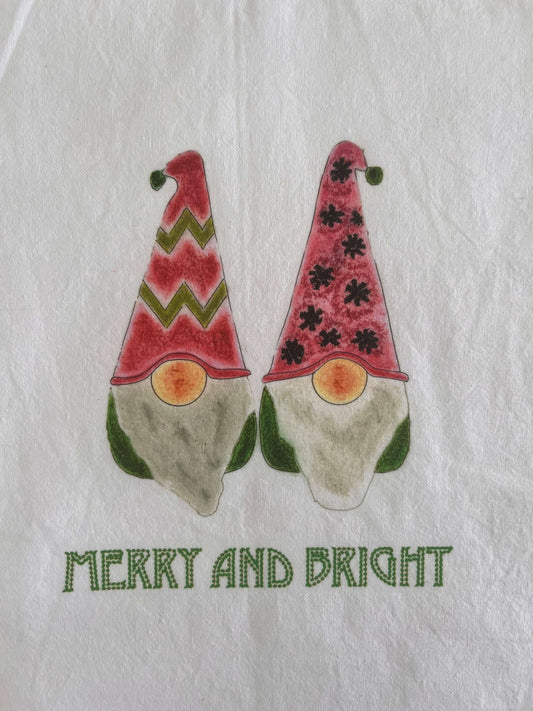 Festive tea towel with two watercolor gnomes in red hats, green accents, and 'Merry and Bright' text.