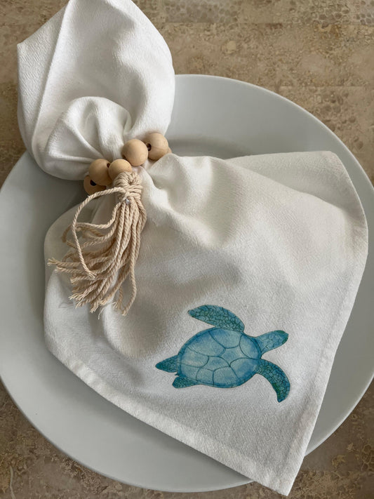 Cotton napkin with blue sea turtle illustration and wooden bead napkin ring on a white plate
