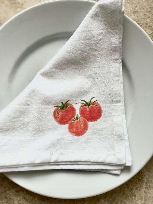 Tomato cotton napkin set displayed on a white plate with hand-drawn tomatoes in red and green colors.