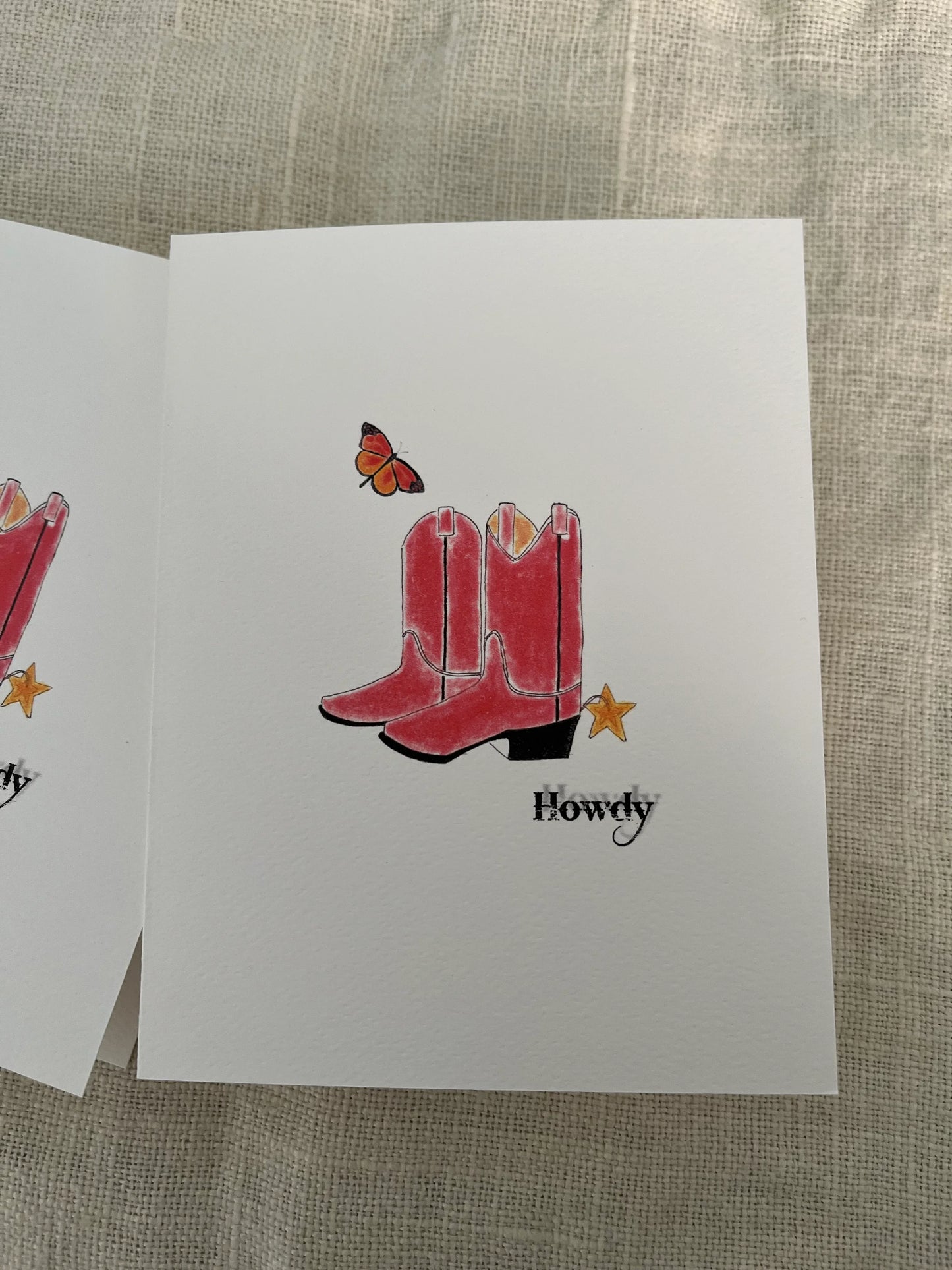 Illustrated greeting card with red cowboy boots, a butterfly, star, and 'Howdy' text on linen.
