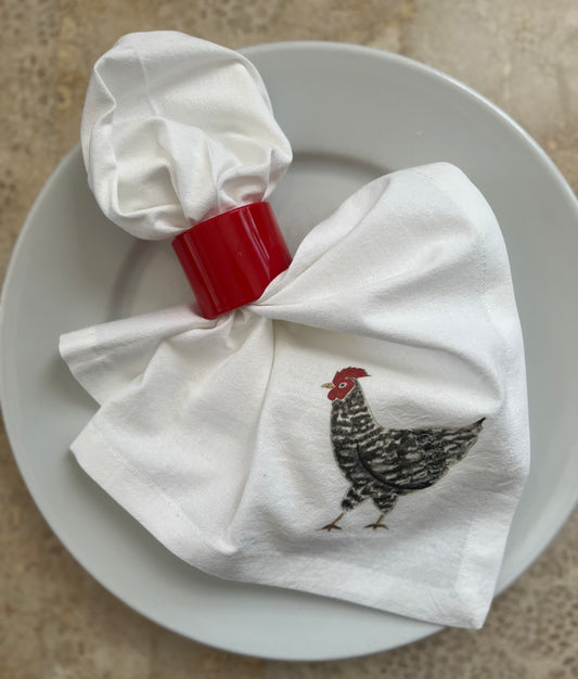Cotton napkin with chicken illustration in a red napkin ring on white plate