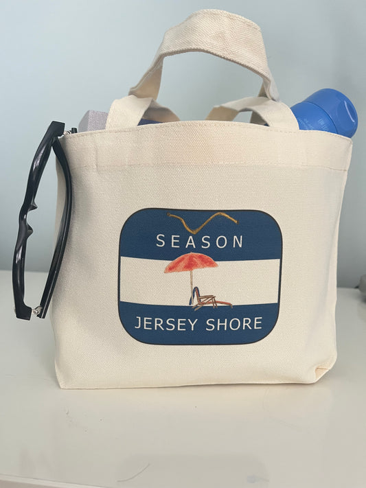 Beach tote bag with 'Season Jersey Shore' design, featuring a red umbrella and chair, perfect for summer outings.
