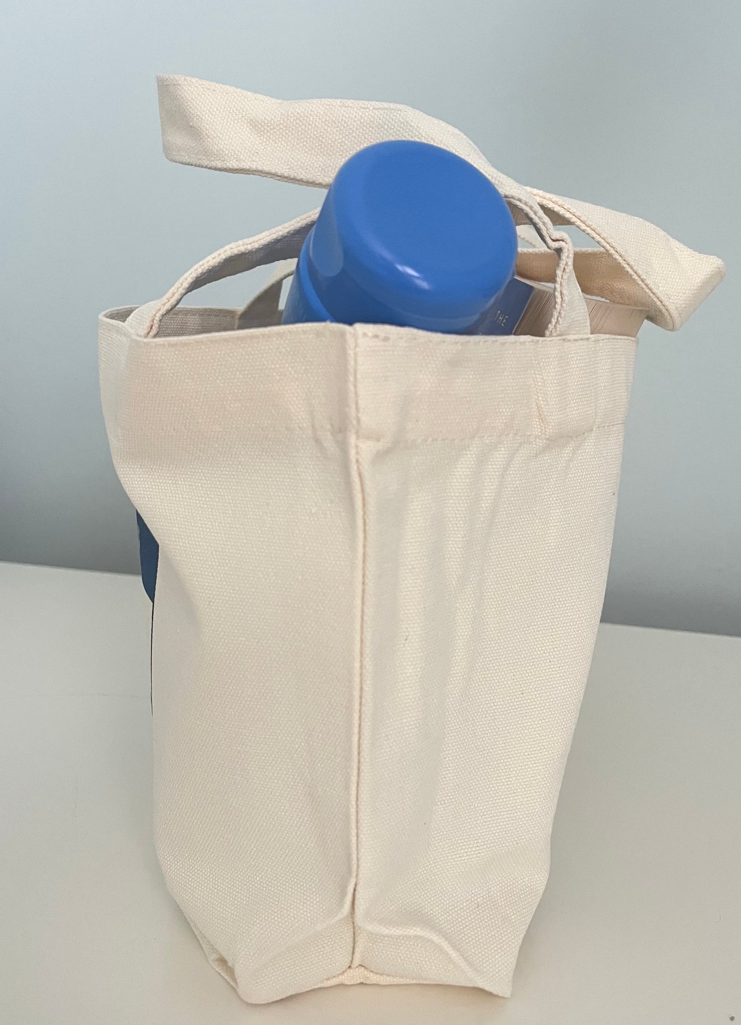 Natural canvas tote bag holding a blue water bottle, perfect for eco-friendly shopping or daily use.