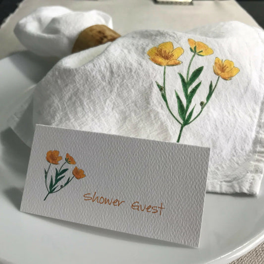 Eco-friendly cloth napkin with yellow flower illustration and matching shower guest place card on plate