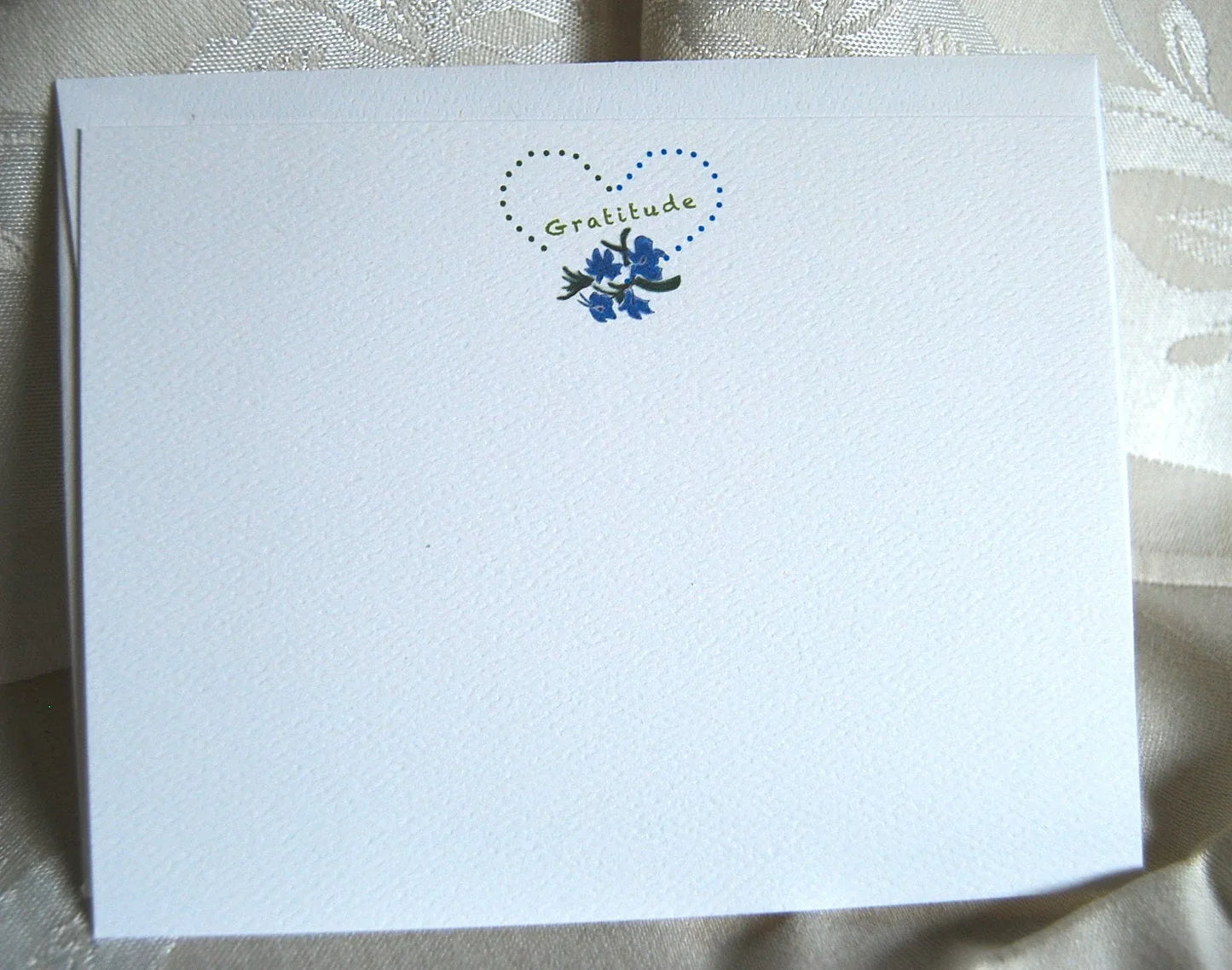 Blank note card with 'Gratitude' text, heart outline, and blue floral illustration at top