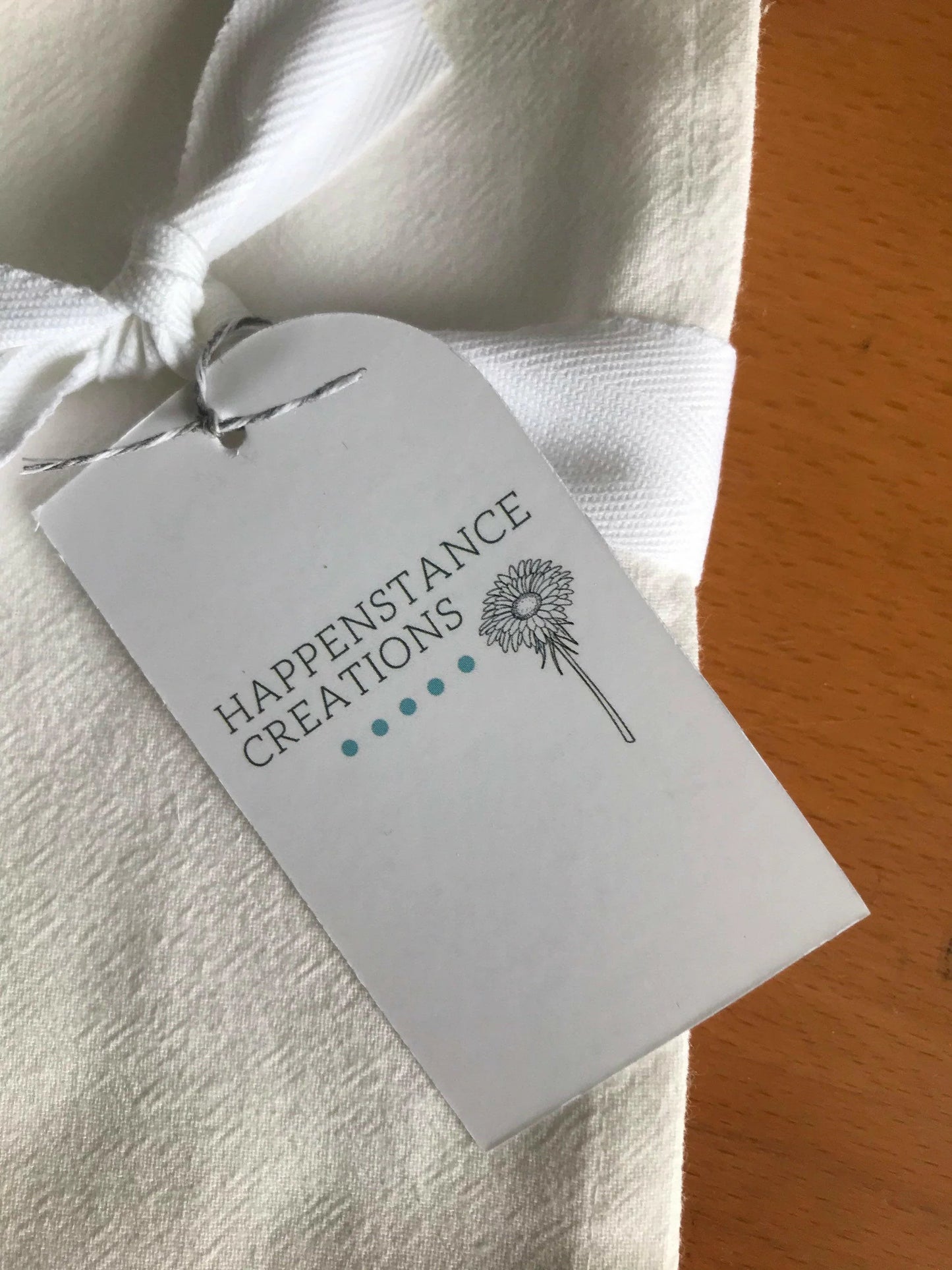 White cotton tea towel with bow and botanical gift tag on wooden surface