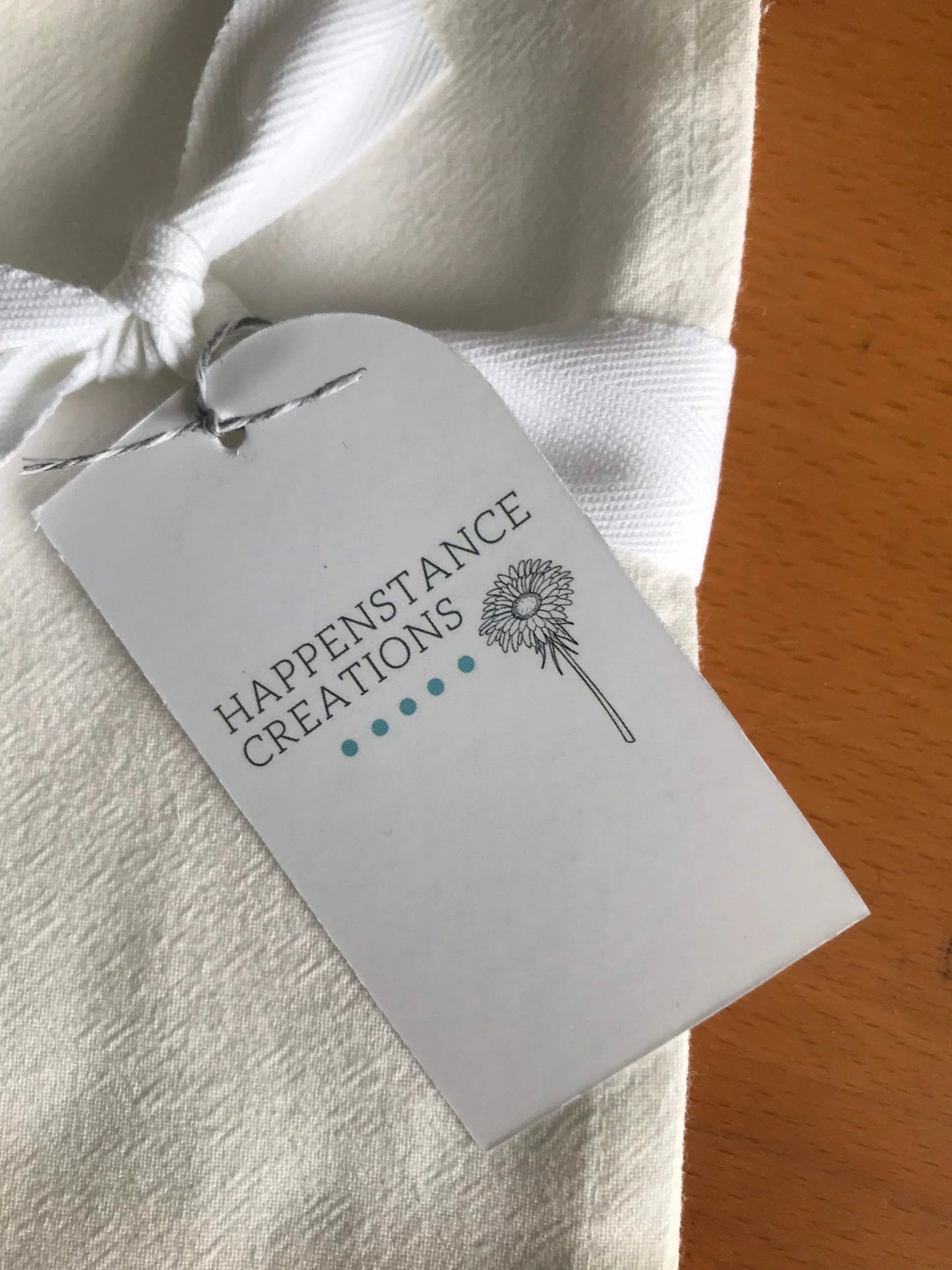 White cotton tea towel with bow and floral gift tag on wooden surface