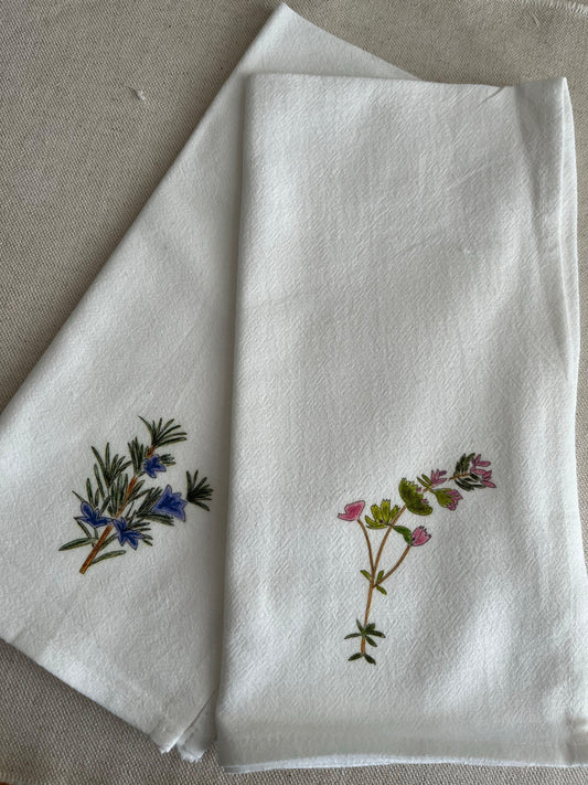 White cotton napkins with hand-drawn botanical floral illustrations on a neutral fabric background