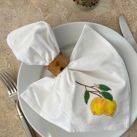 White cotton napkin with hand-painted lemon design in a wooden ring on a dinner plate