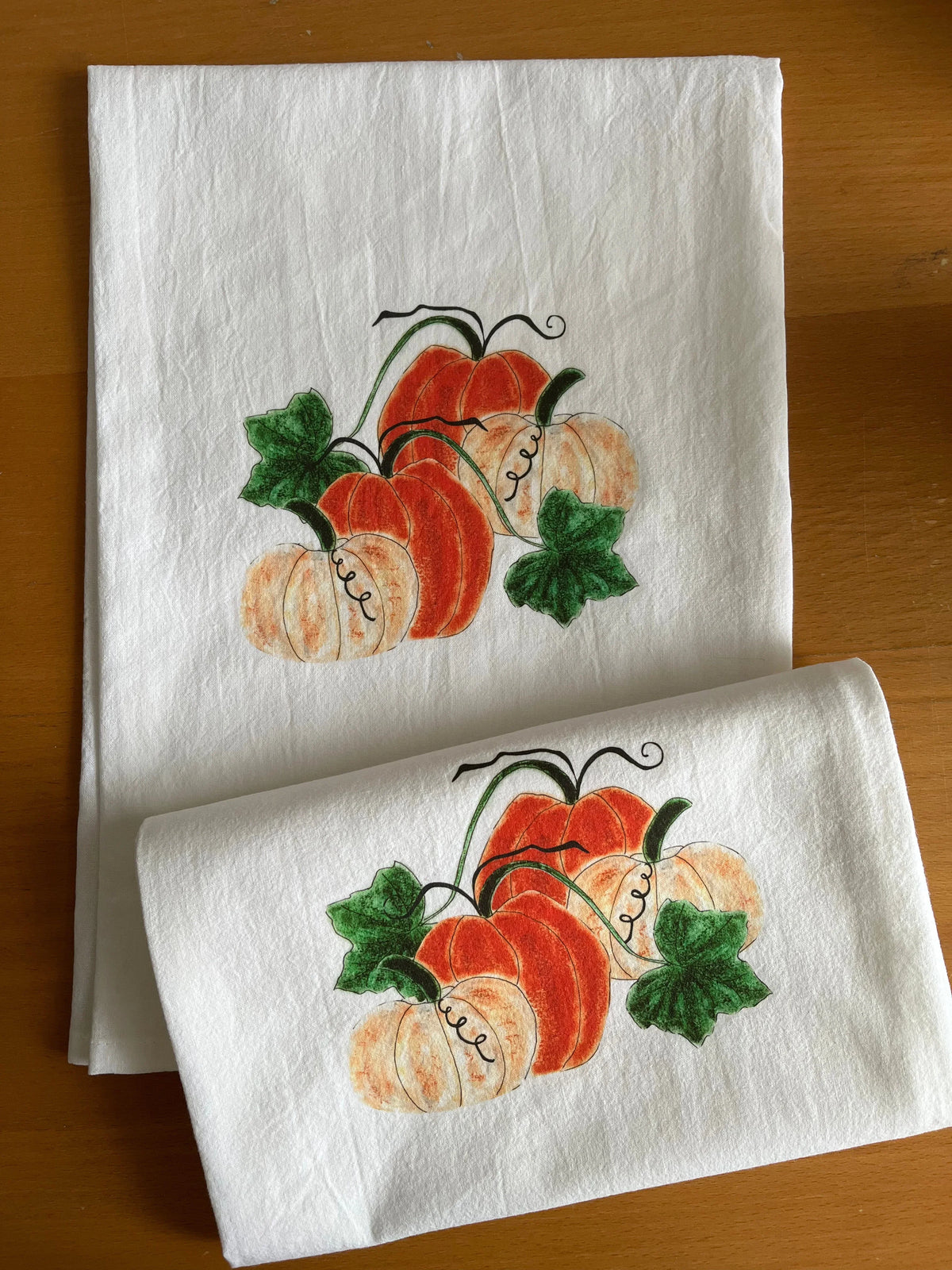 Autumn pumpkin tea towels with illustrated orange and cream pumpkins, green leaves on white cotton
