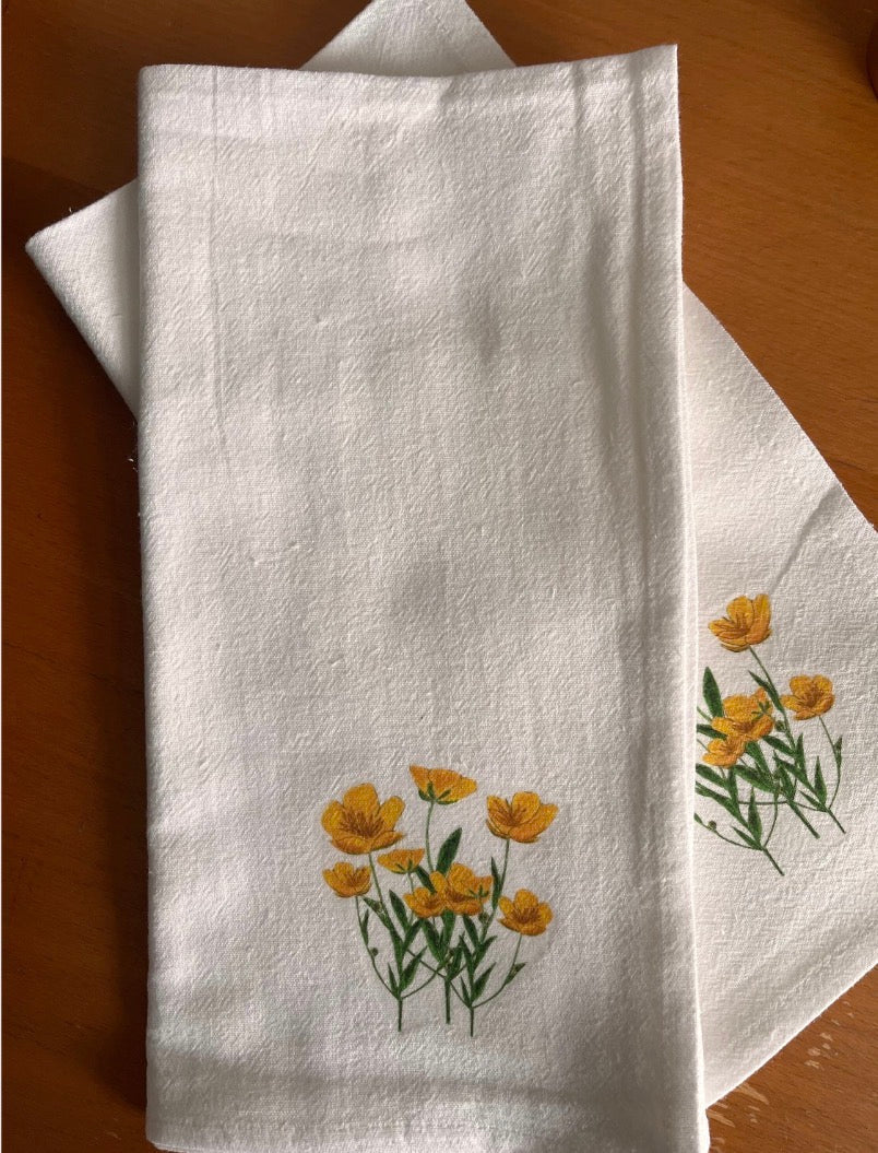 White cotton napkins with yellow wildflower illustration on wooden table