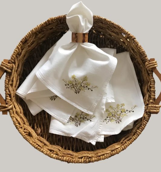 White cotton napkins with botanical print displayed in woven basket, nature-inspired table linens