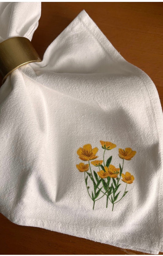 White cloth napkin with hand-illustrated yellow floral design and gold napkin ring