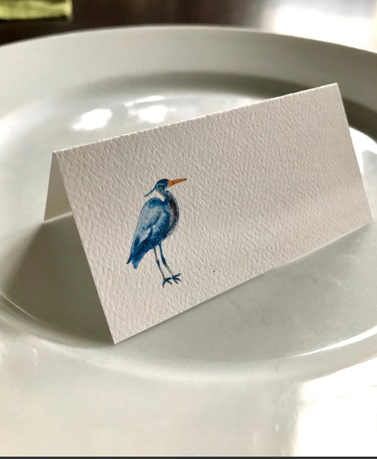 Hand-illustrated place card with blue heron watercolor on a white plate, eco-friendly event decor