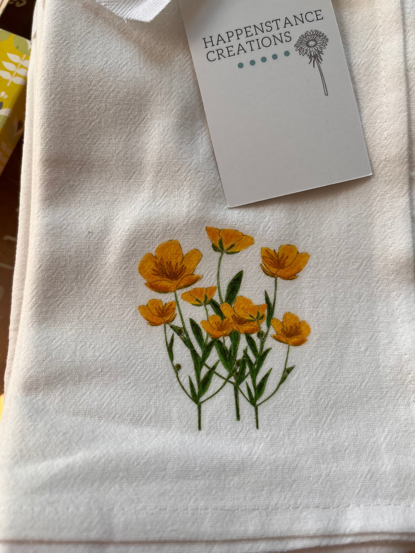 White cotton tea towel with yellow wildflower illustration and product tag