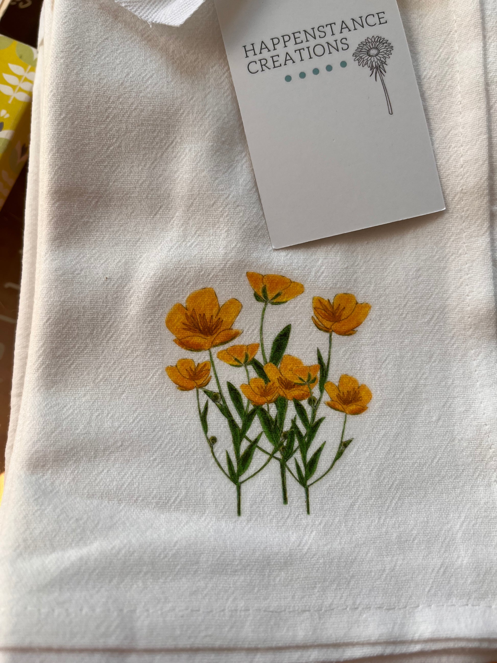 White cotton tea towel with yellow wildflower illustration and product tag