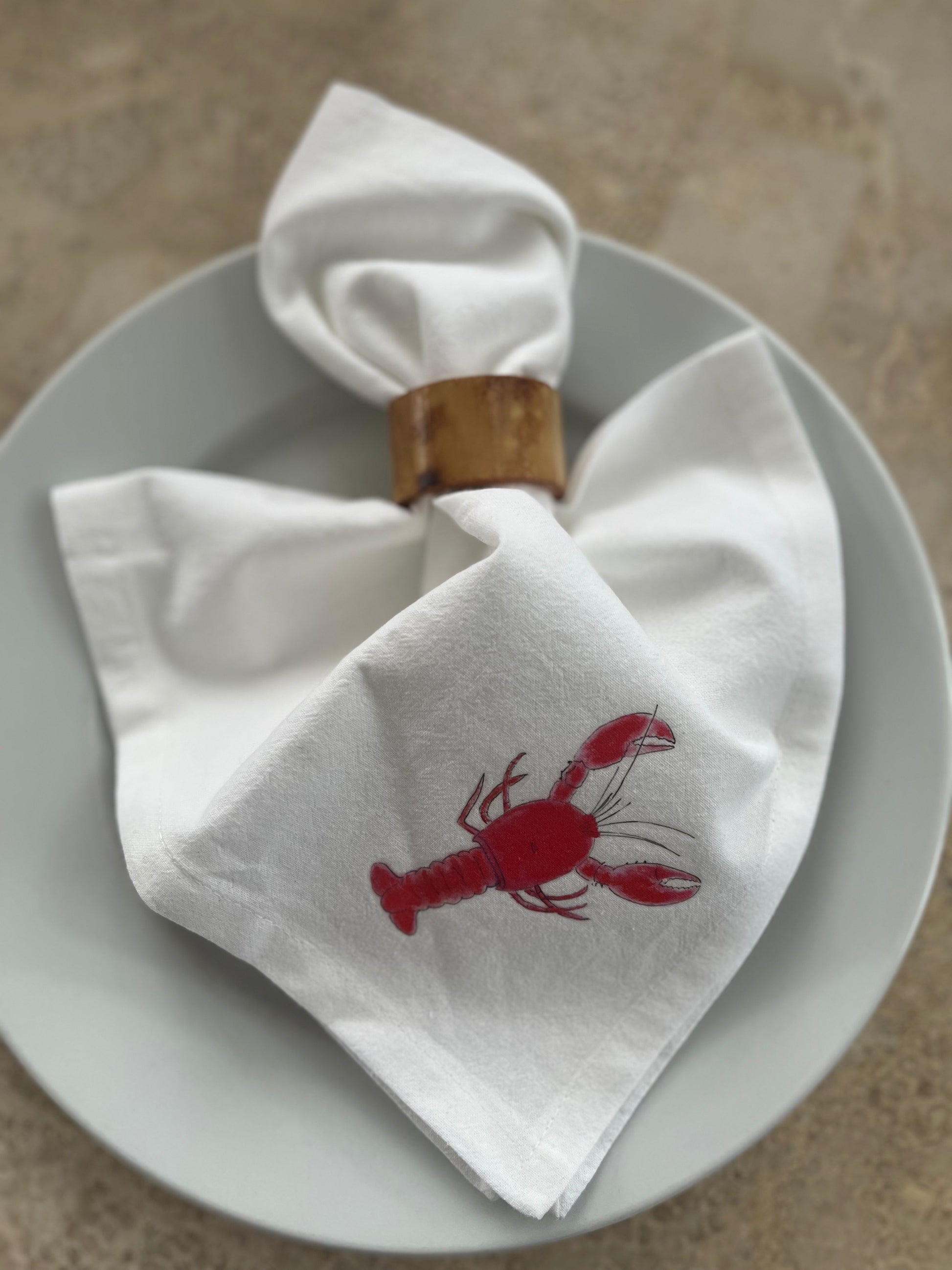 White cotton napkin with red lobster illustration in a wooden ring on a plate
