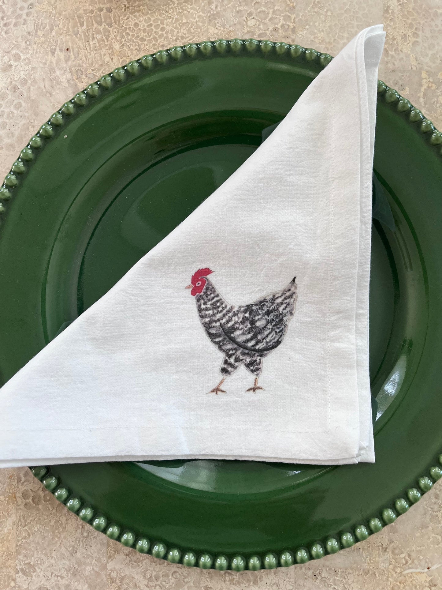 White cotton napkin with illustrated chicken on green beaded plate, nature-inspired table setting