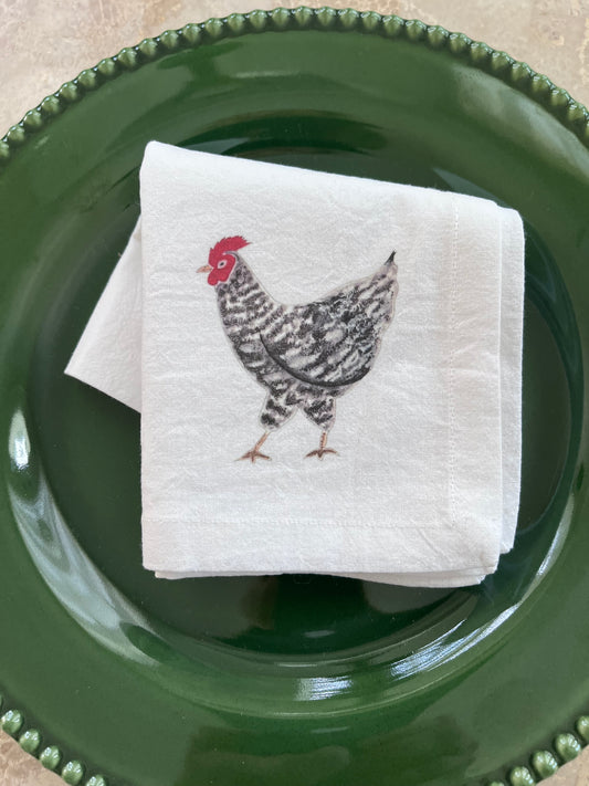 White cotton napkin with illustrated rooster, placed on green beaded plate for farmhouse table setting
