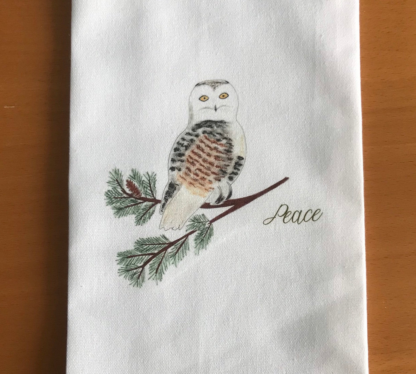 Illustrated tea towel with snowy owl on pine branch and 'Peace' text