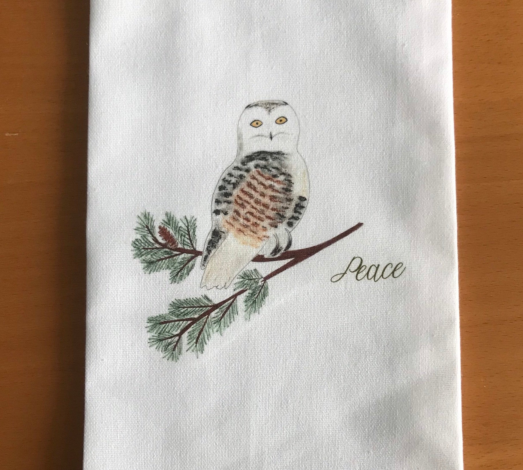 Illustrated tea towel with snowy owl on pine branch and 'Peace' text