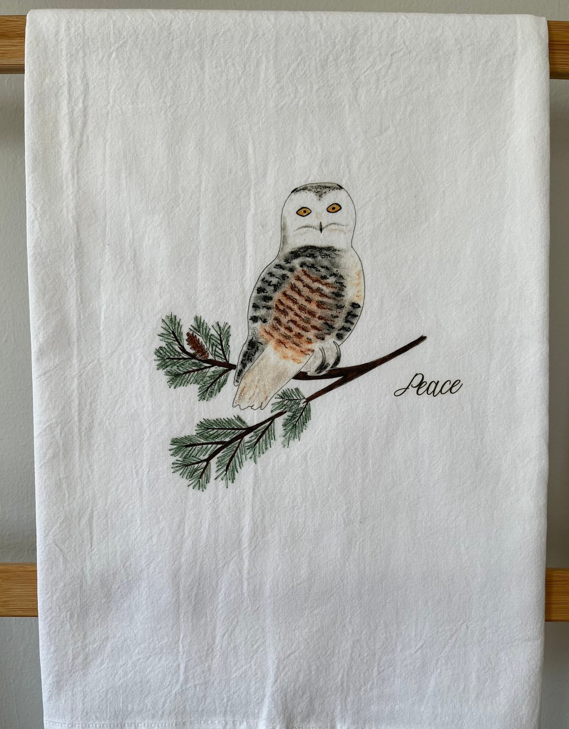 Illustrated tea towel with snowy owl on pine branch and 'Peace' text, nature-inspired decor