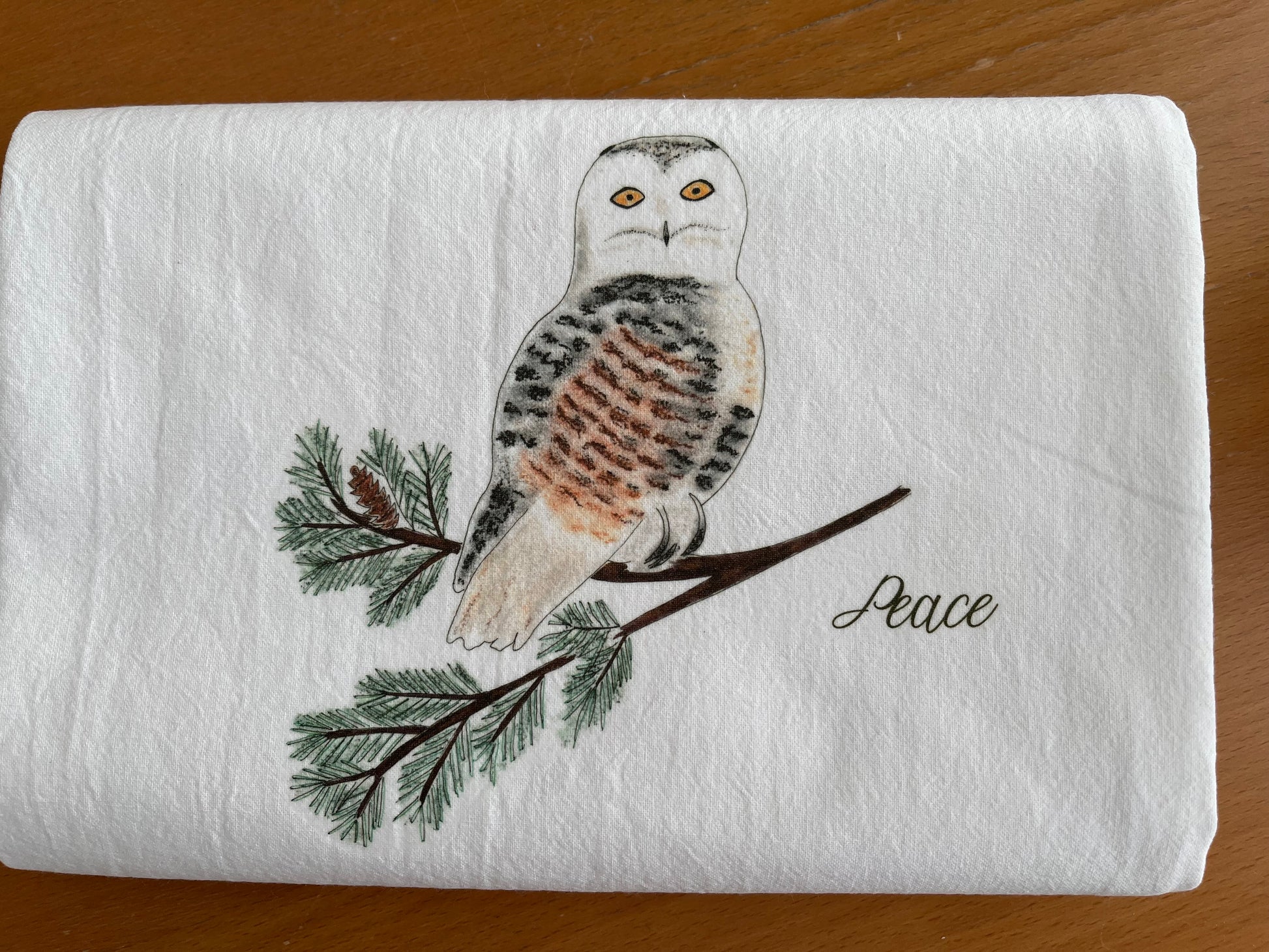 Illustrated snowy owl on pine branch with 'Peace' text on white cotton tea towel