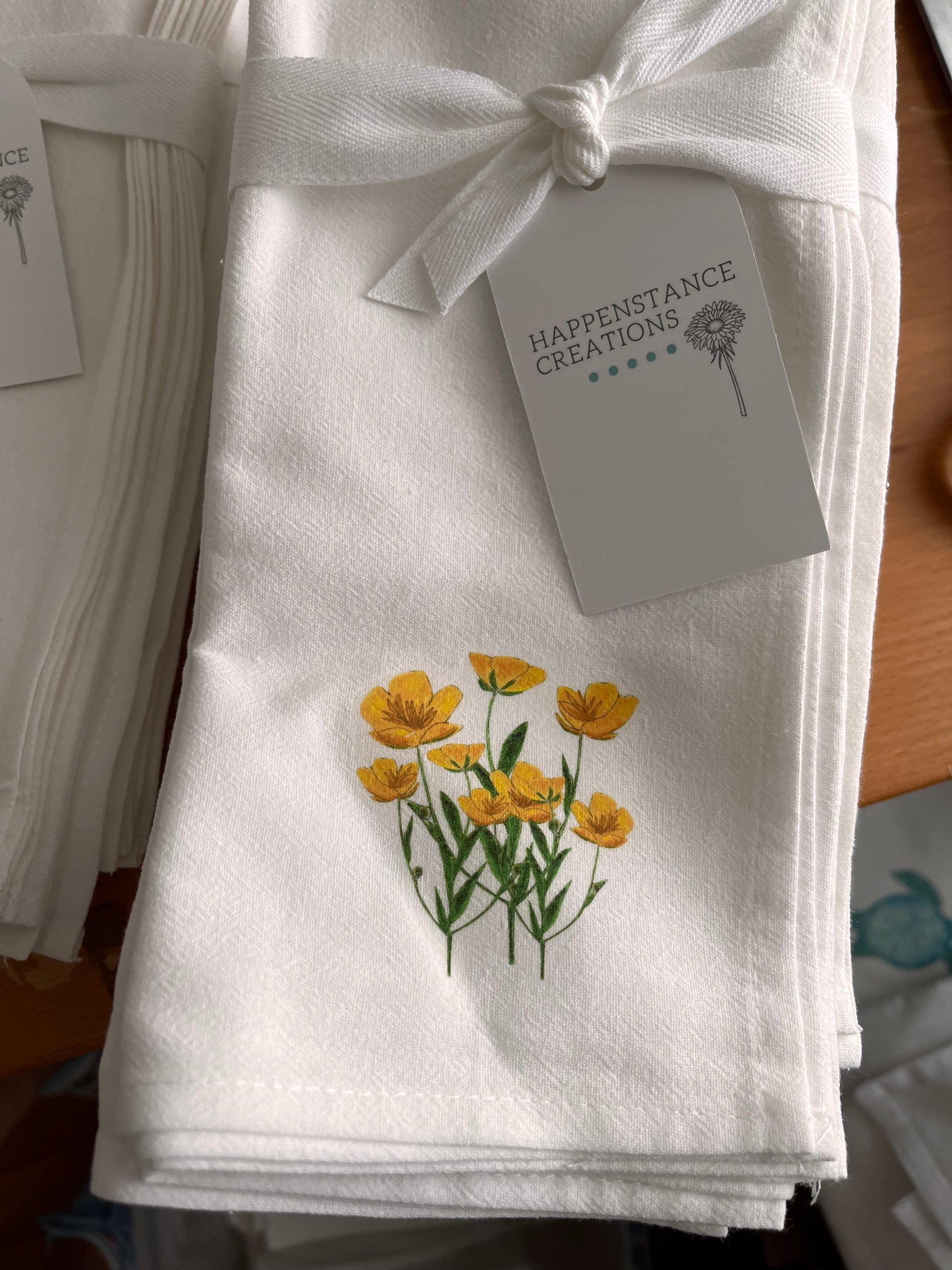 White cotton napkin with yellow flower illustration, tied with a bow and displayed with tag