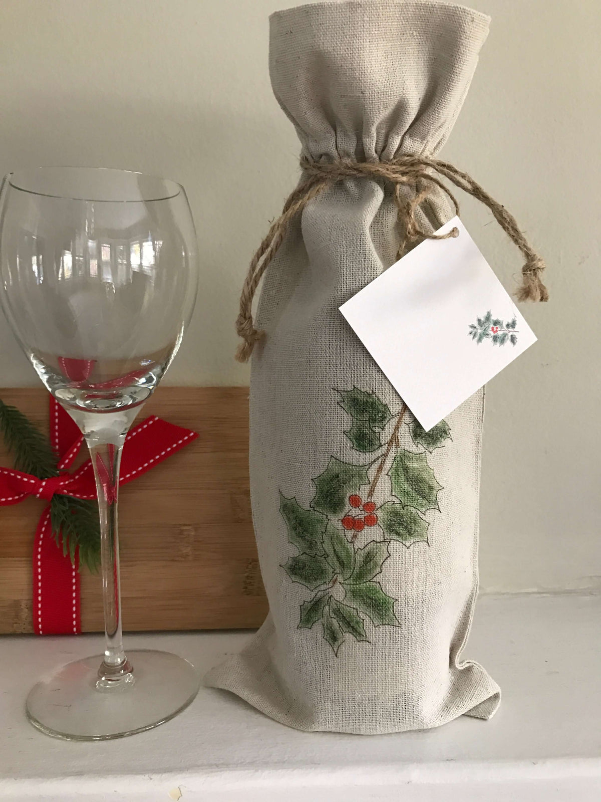 Holiday Linen Wine Bag Trio Set with Gift Card Set featuring holly design and matching gift tag next to a wine glass.
