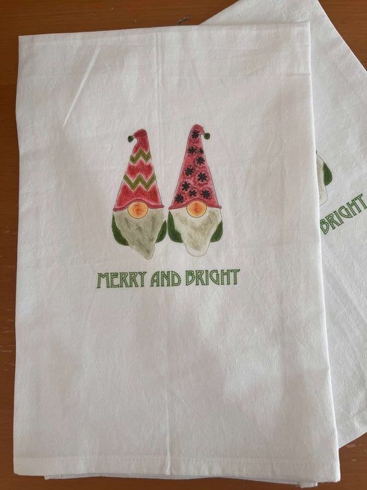 White tea towel with two festive gnomes in red hats, green accents, and 'Merry and Bright' text—perfect for holiday gatherings.