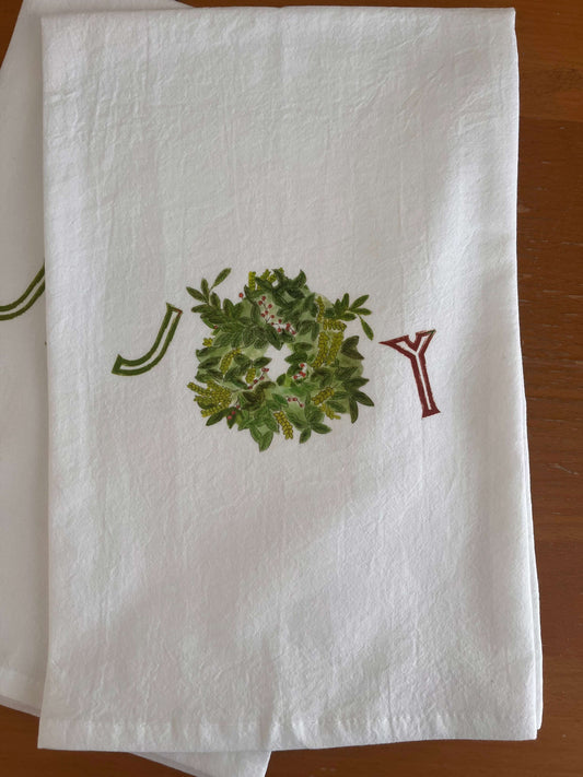 White tea towel with 'JOY' design, green wreath, and red lettering for festive gatherings