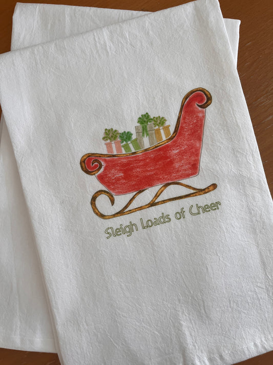 White tea towel with red sleigh illustration carrying potted plants, text 'Sleigh Loads of Cheer', festive holiday design