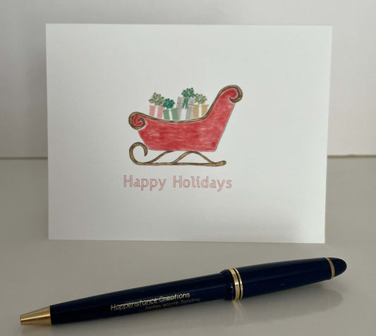 Holiday note card with red sleigh illustration and 'Happy Holidays' text, paired with a pen for writing.