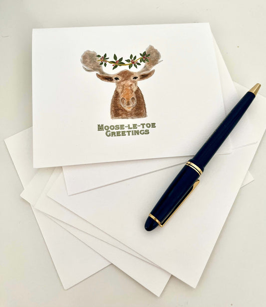Moose illustration note card with 'Moose-le-toe Greetings' text, white envelopes, and blue pen