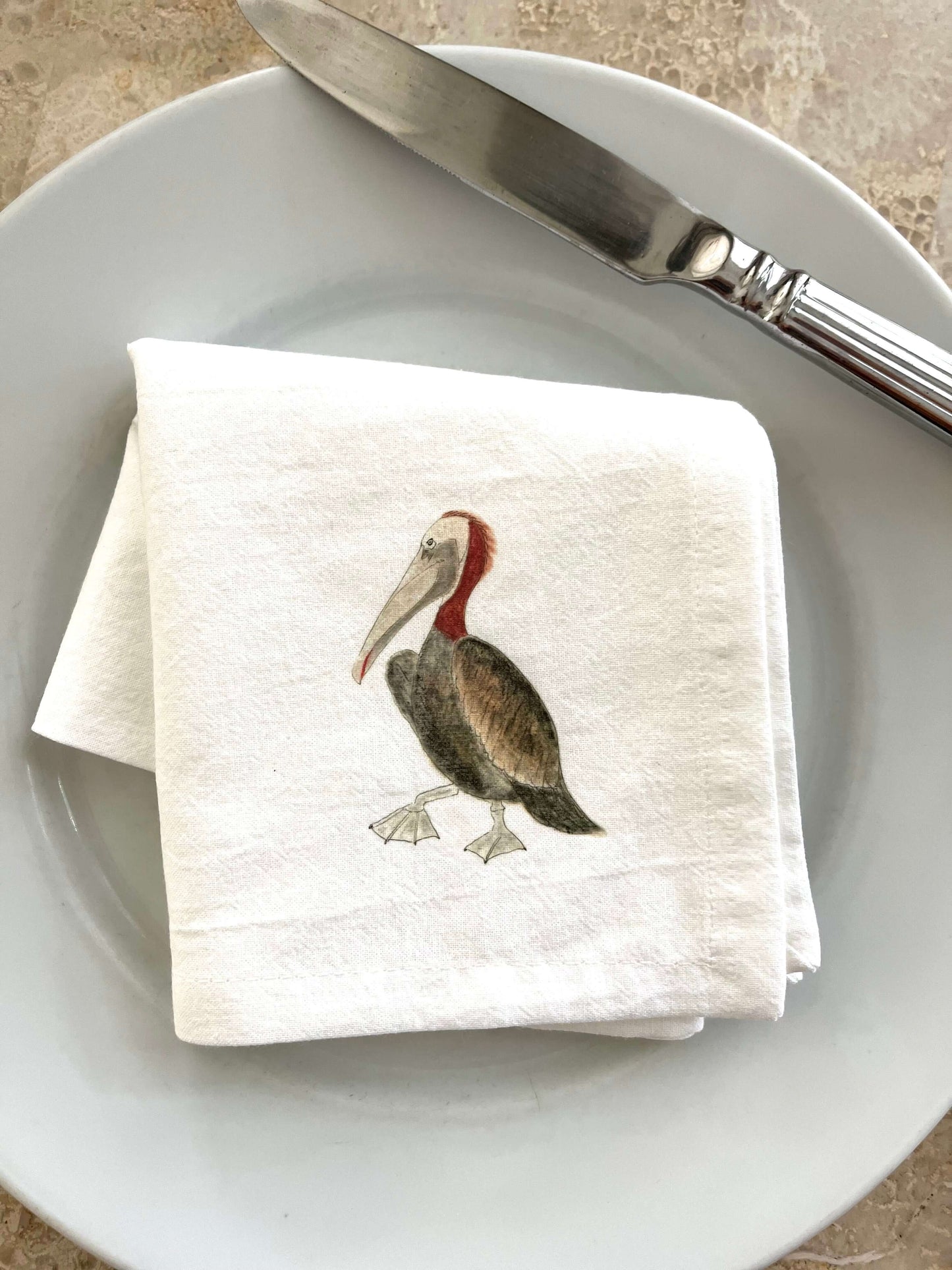 Pelican napkin set on a white plate, featuring an illustrated pelican design, perfect for coastal-themed dining.