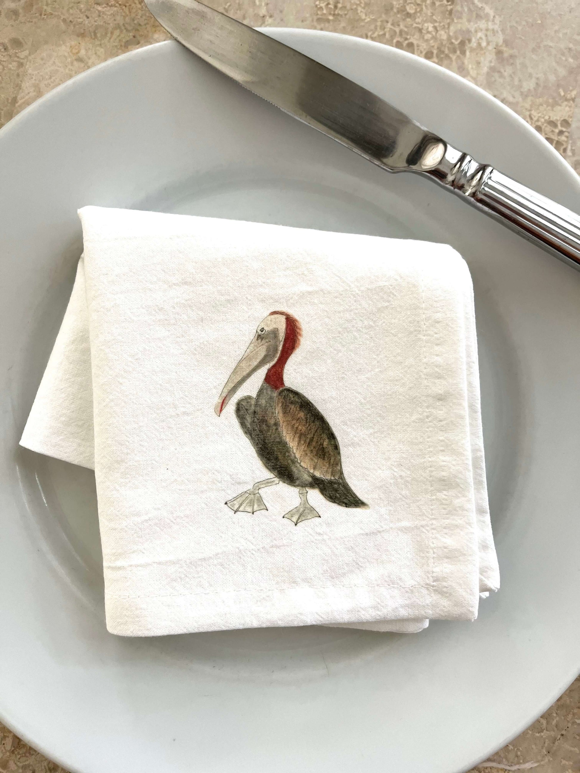 Pelican napkin set on a white plate, featuring an illustrated pelican design, perfect for coastal-themed dining.