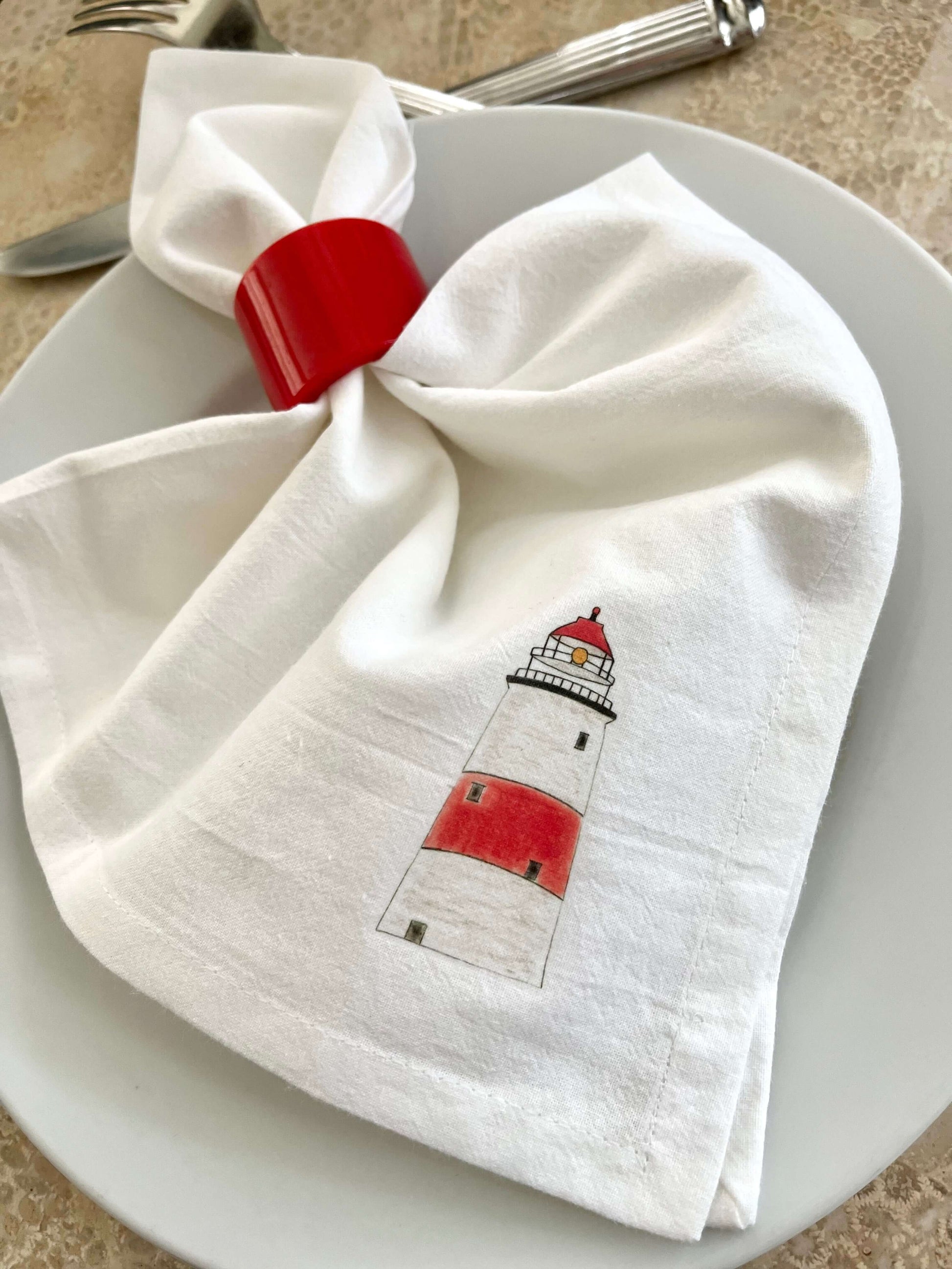 Lighthouse napkin set featuring hand-illustrated lighthouse artwork on a white cloth napkin, perfect for coastal dining.