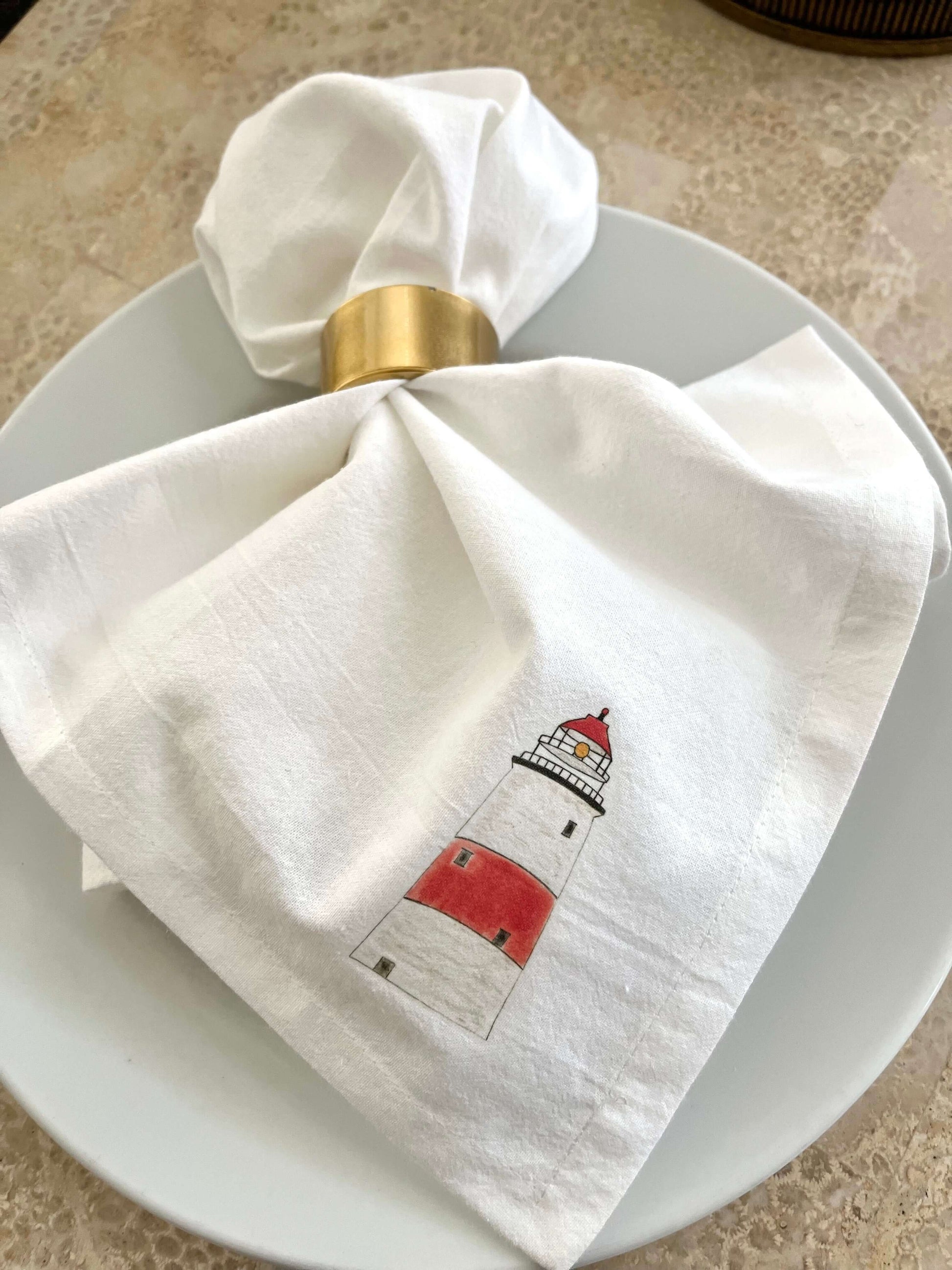 Lighthouse Napkin Set featuring hand-illustrated lighthouse artwork on a white napkin, perfect for coastal dining.