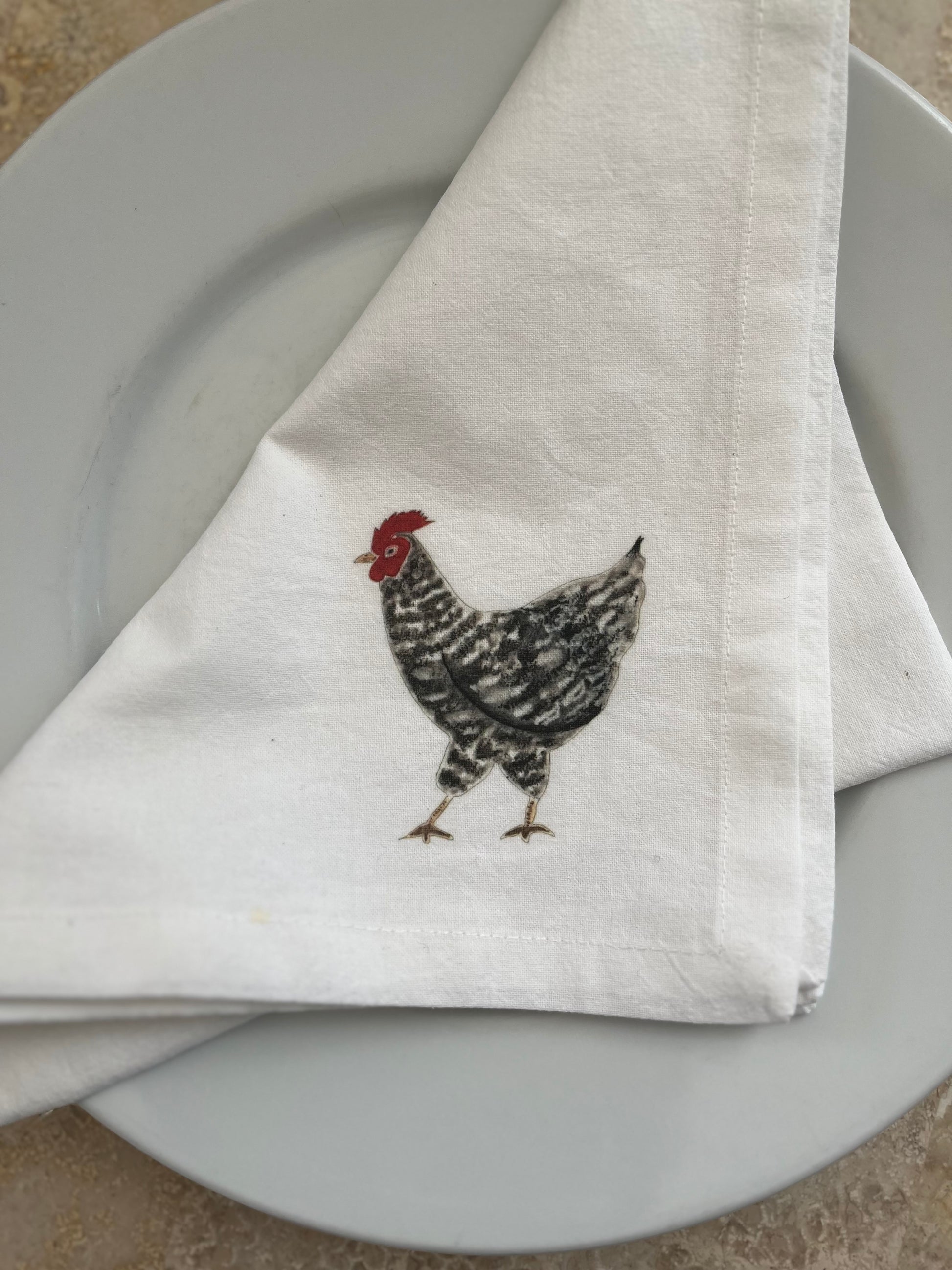Cotton napkin with illustrated chicken design on a white dinner plate
