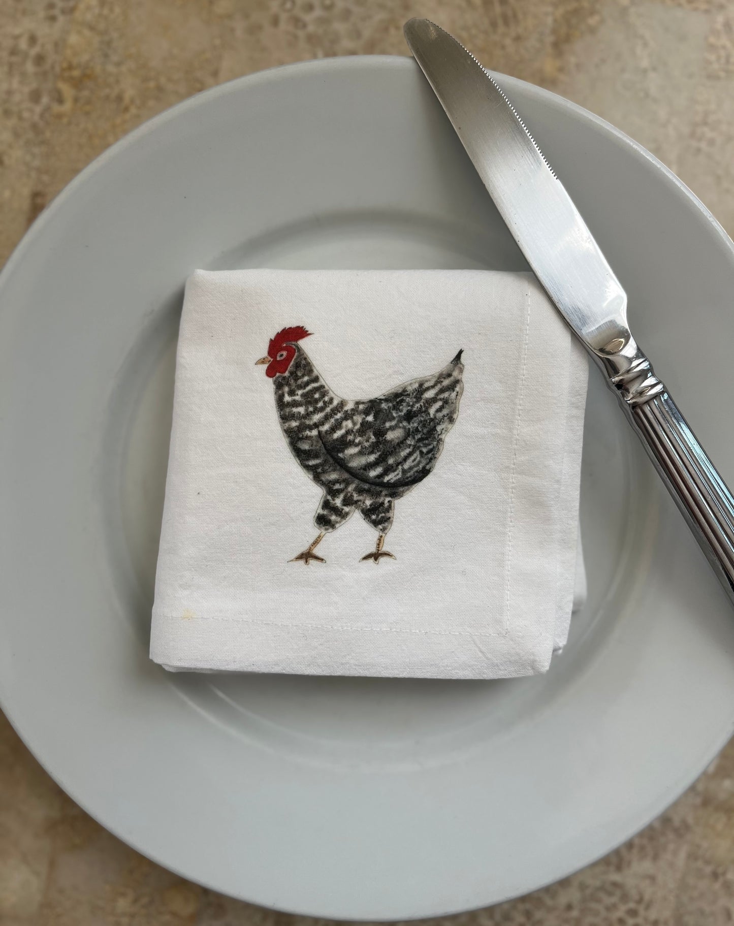 Illustrated chicken cotton napkin on plate with knife, rustic table setting