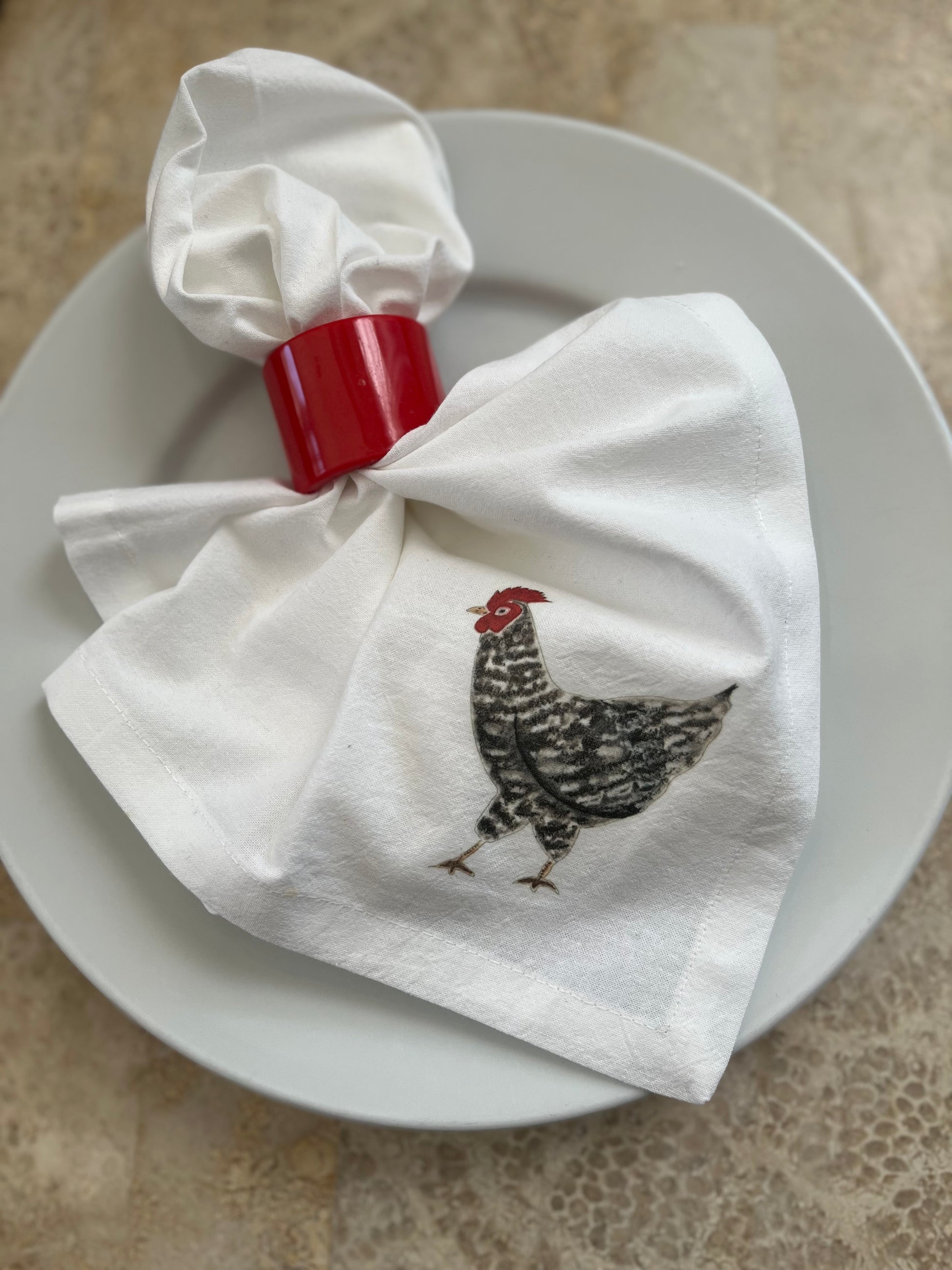 Cotton napkin with illustrated black and white chicken, red napkin ring on white plate