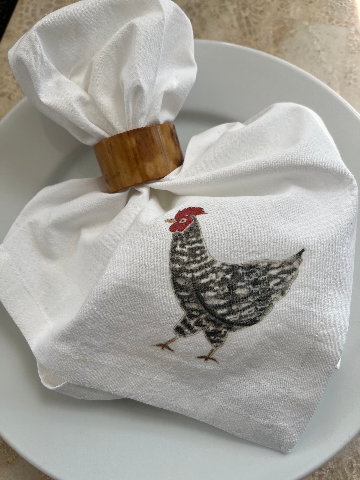 Cotton napkin with illustrated chicken design in wooden napkin ring on white plate