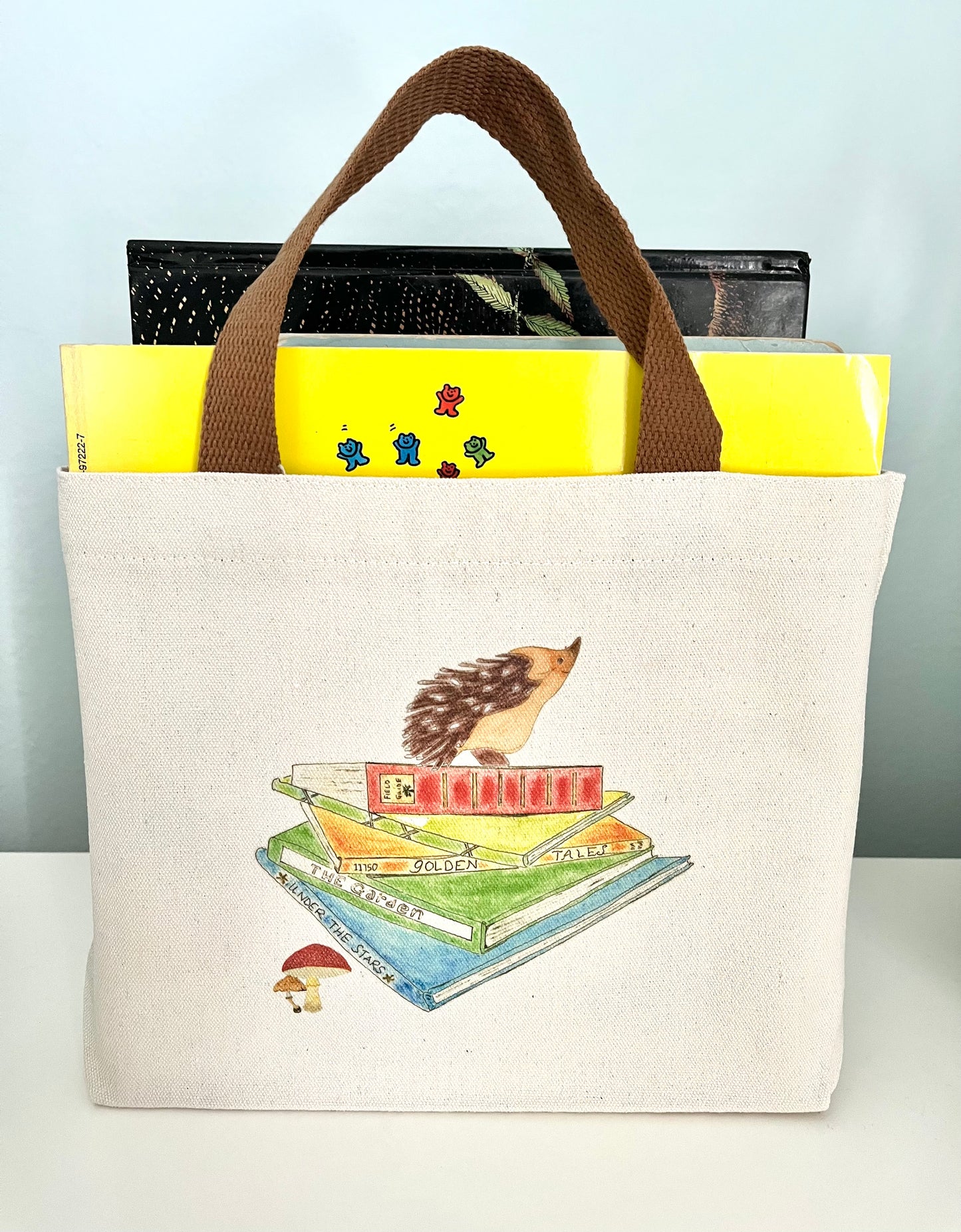 Canvas tote bag with illustrated hedgehog and books, filled with colorful books