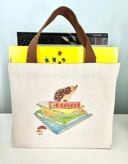 Canvas tote bag with illustrated hedgehog and books, filled with colorful books