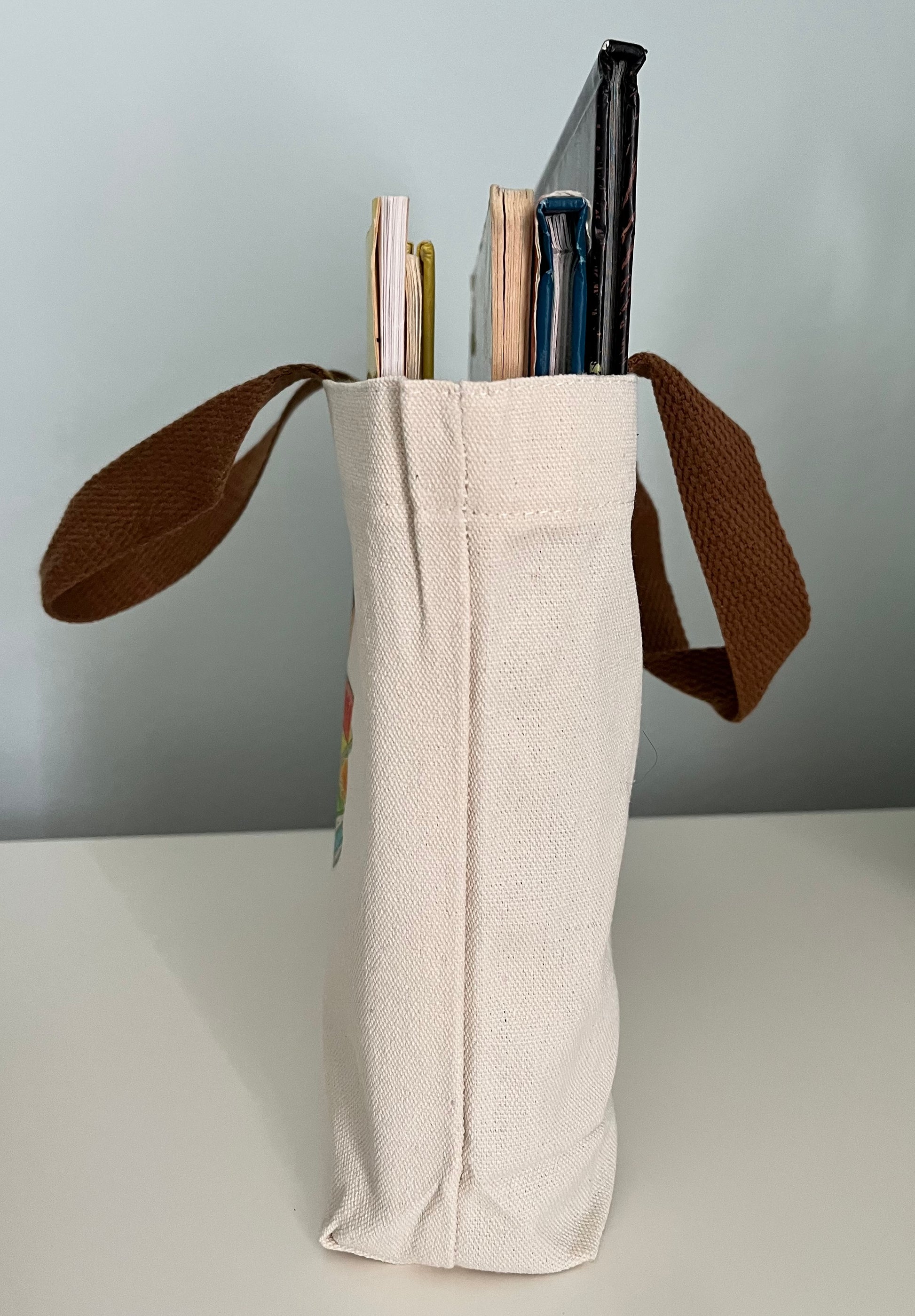 Cotton canvas tote with brown handles holding notebooks and journals on a white surface