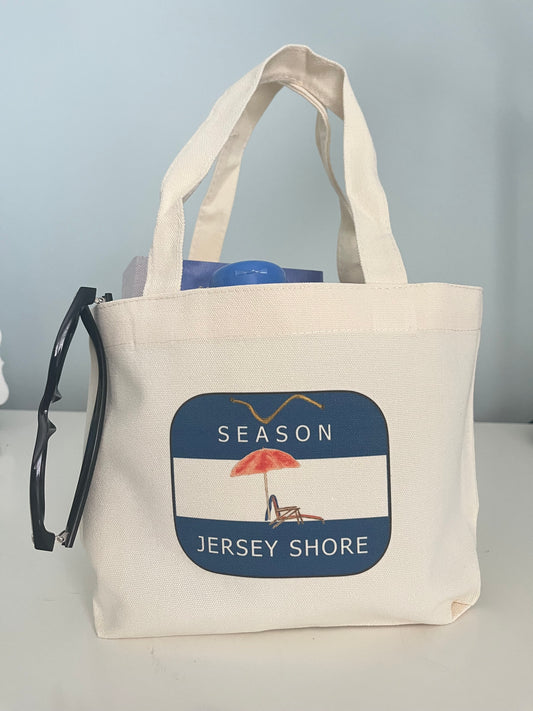 Beach-themed canvas tote bag with 'Season Jersey Shore' design, featuring umbrella and chair illustration for summer outings.