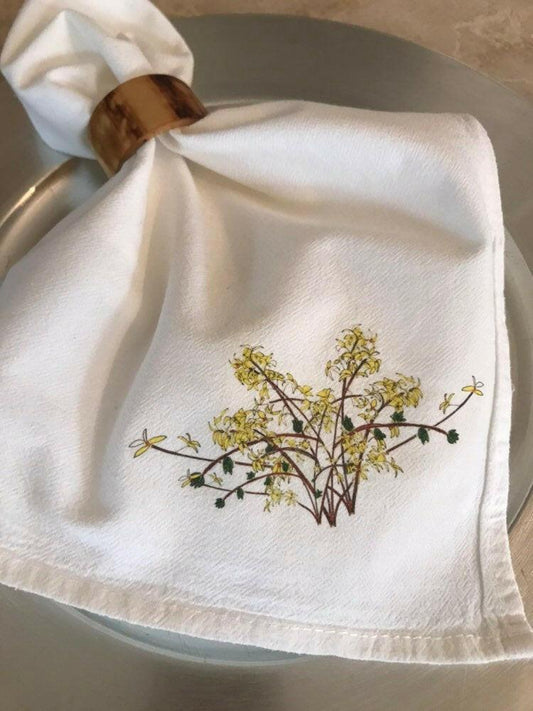 White cotton napkin with yellow floral illustration, wooden napkin ring on silver plate